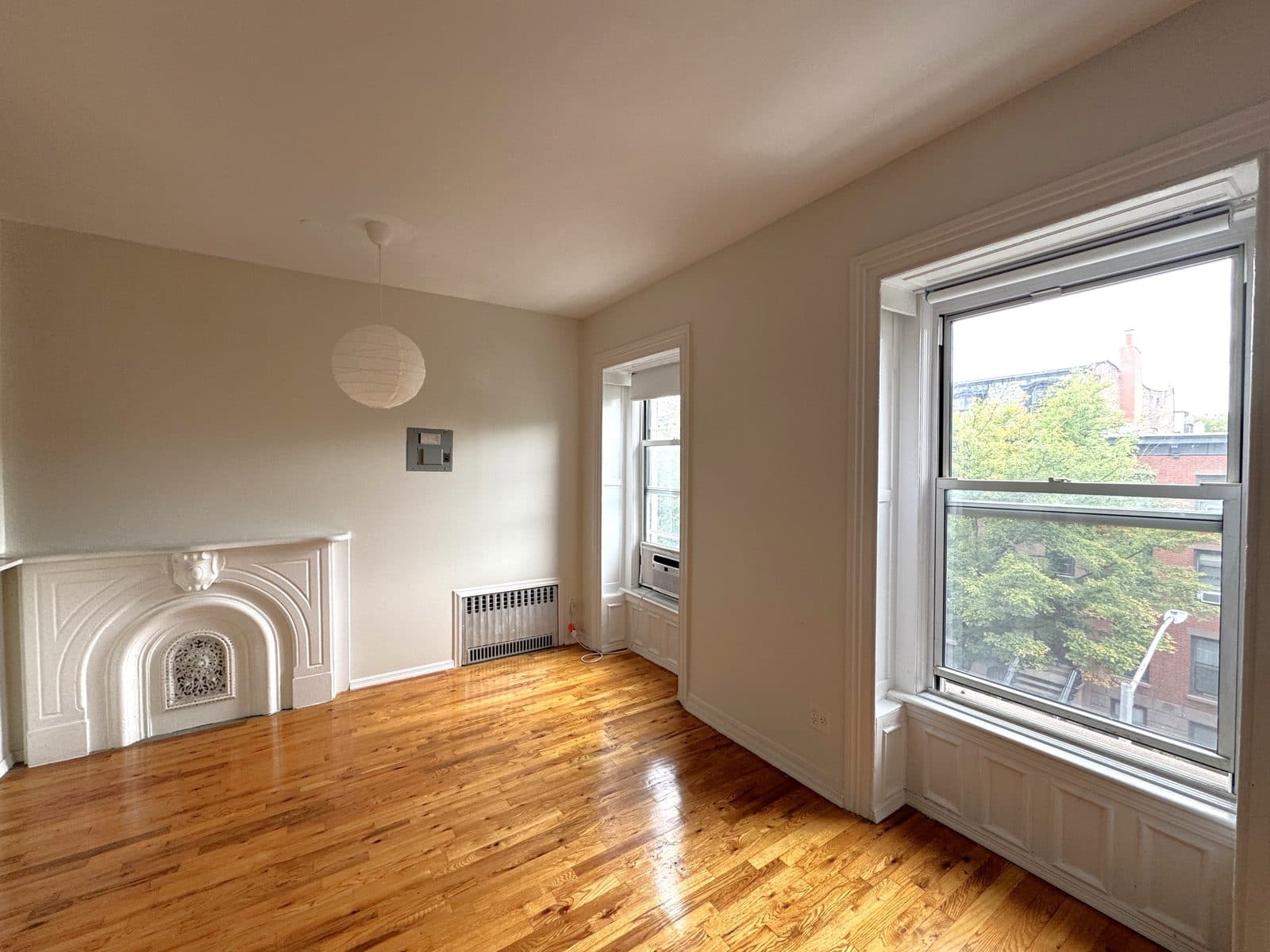 Empty prewar living room with a white marble mantel and tall windows